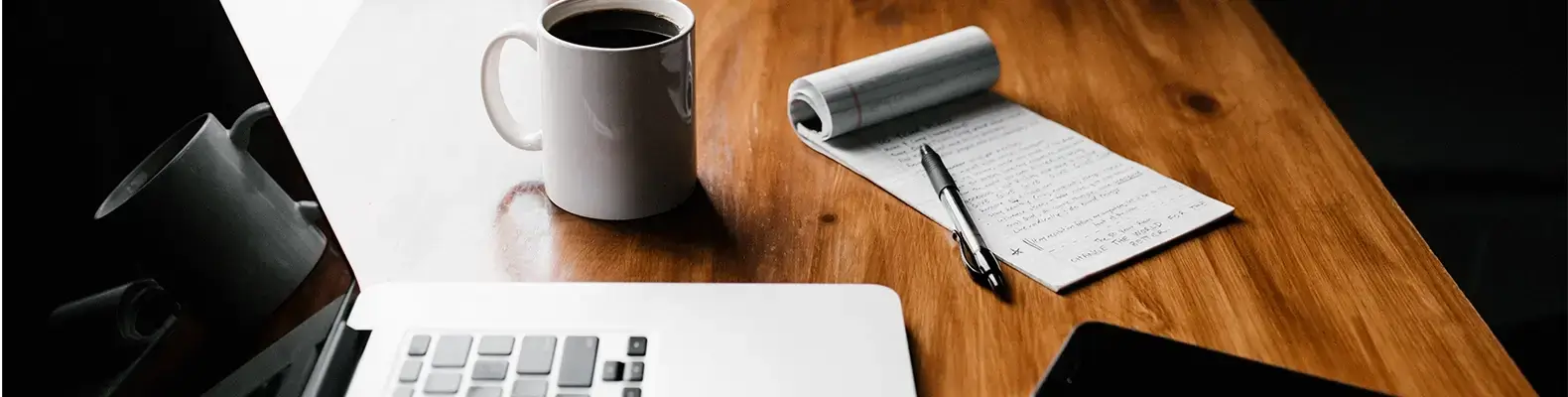 Laptop. Kaffee und ein Notizblock auf einem braunen Bürotisch.